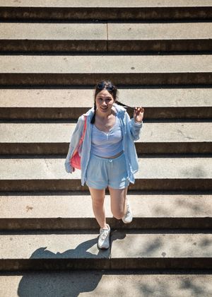 Young Asian woman in light blue outfit descending outdoor concrete stairs on a sunny day.