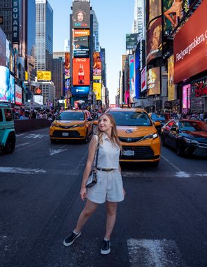 Young woman in white romper posing at a busy Times Square intersection with yellow taxis.