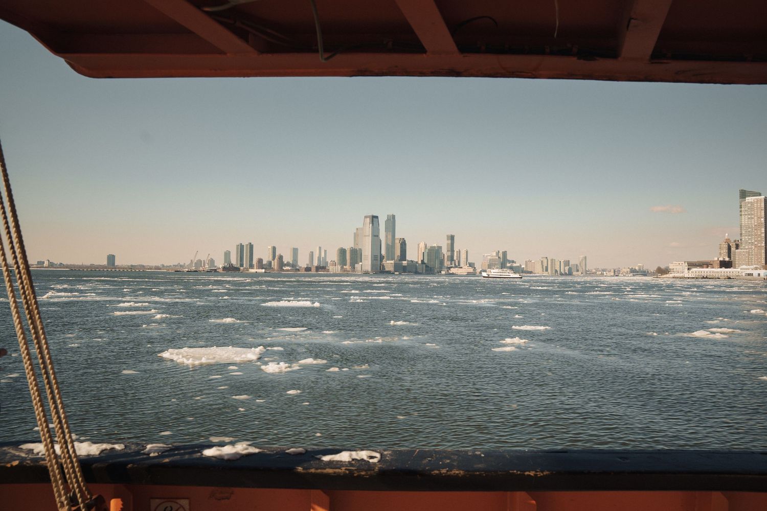 City skyline viewed from boat deck across choppy icy harbor waters on clear sunny day.