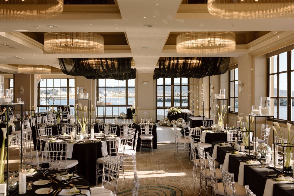Elegant ballroom reception venue with crystal chandeliers, floor-to-ceiling windows, and black and white table settings.