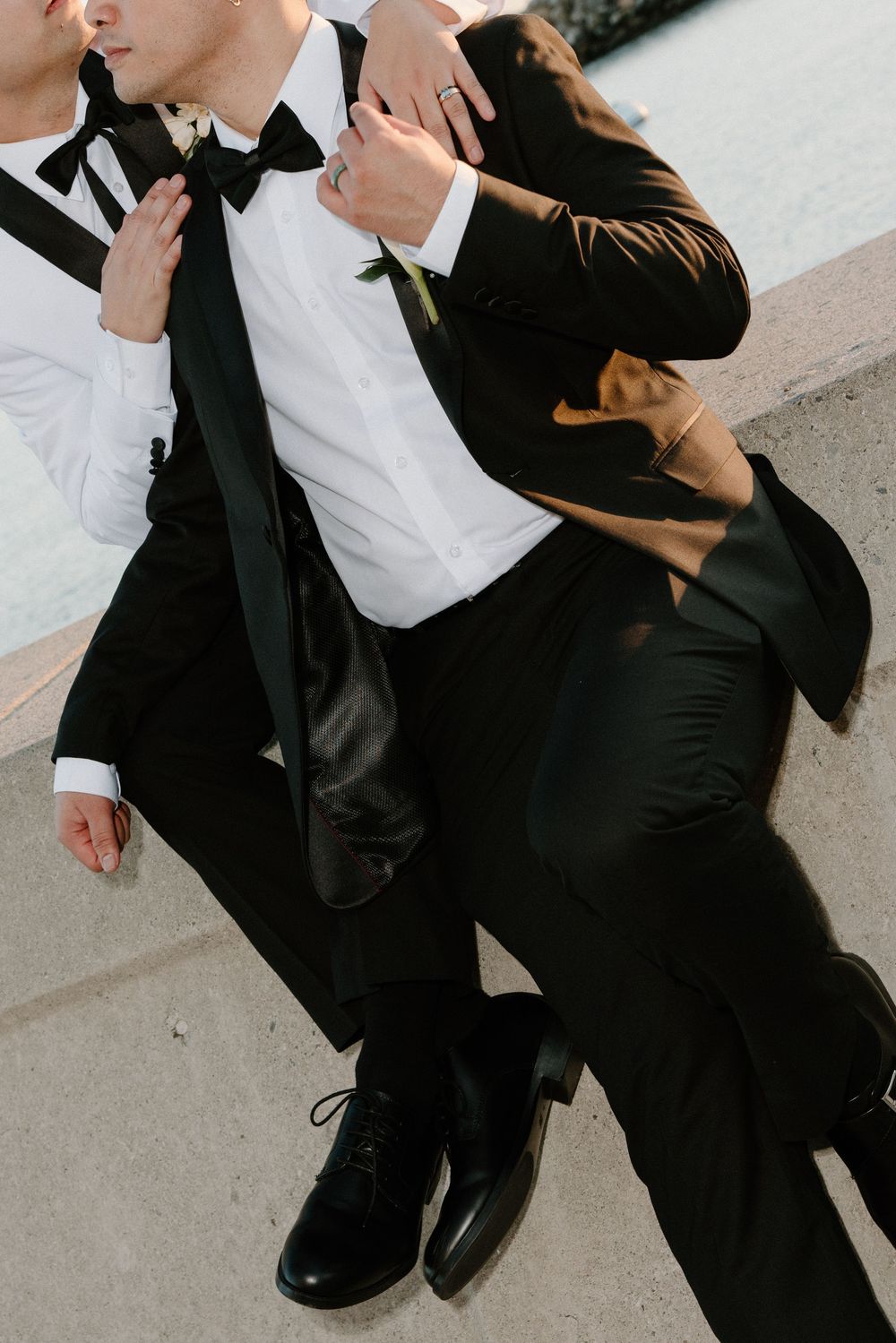 Two figures in formal black and white attire embrace in an intimate dance pose outdoors.