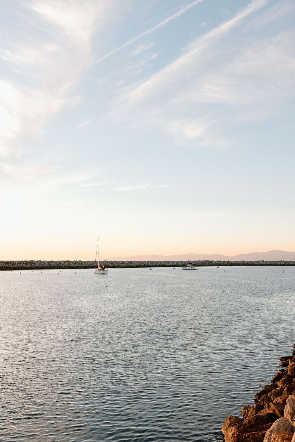 Serene waterfront landscape with boats dotting the calm harbor under a soft sunset sky.