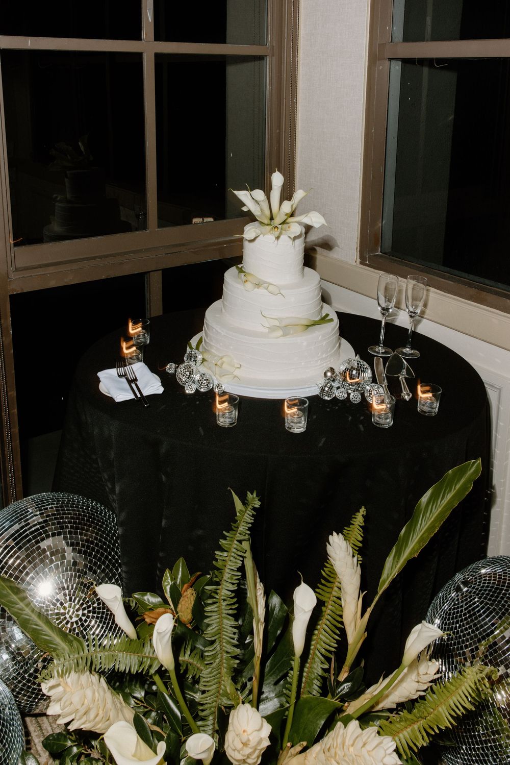 Wedding cake display with white calla lilies and ferns surrounded by crystal decor and ambient lighting.
