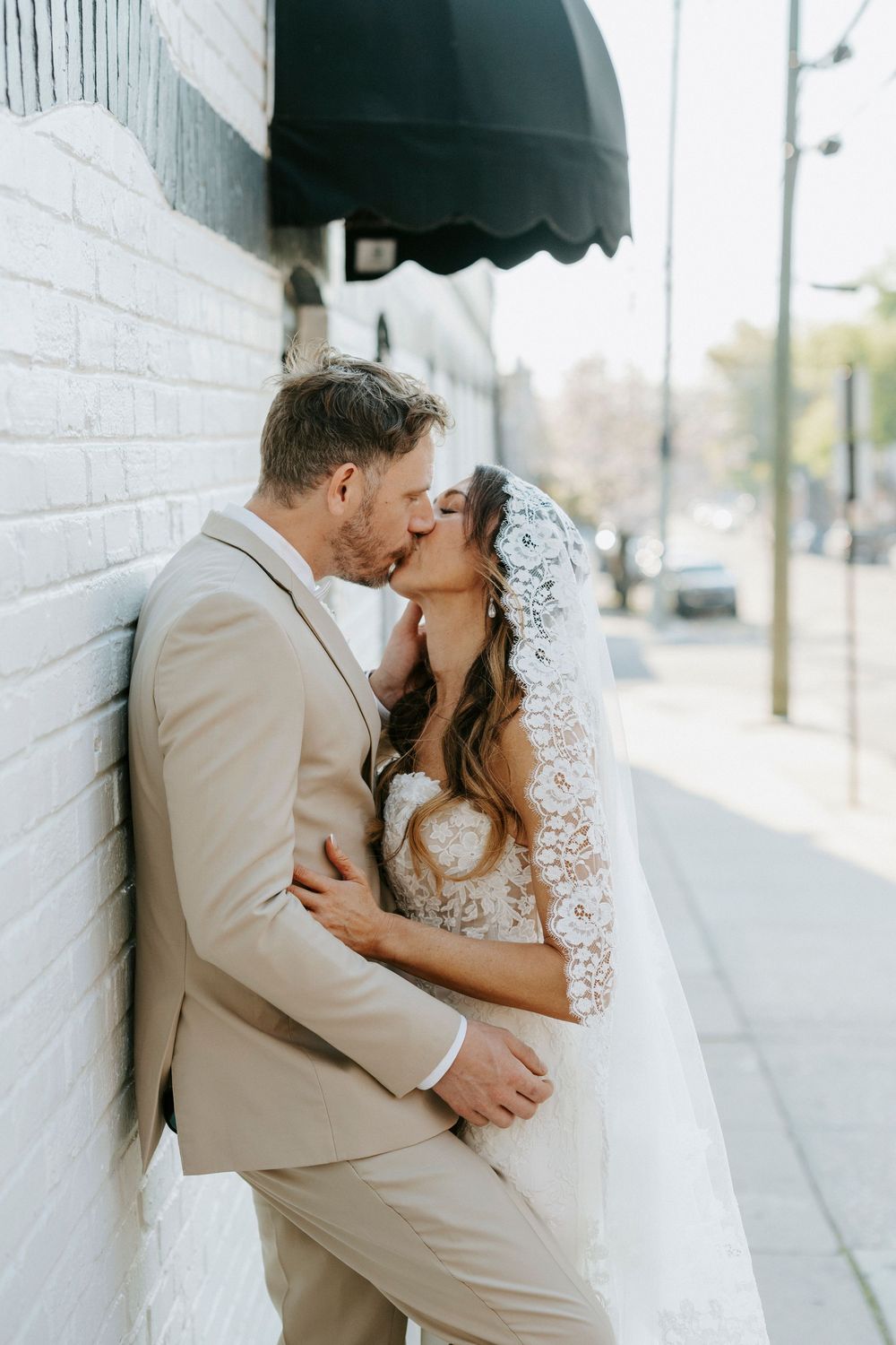 Romantic wedding couple sharing intimate moments against a white brick wall backdrop.