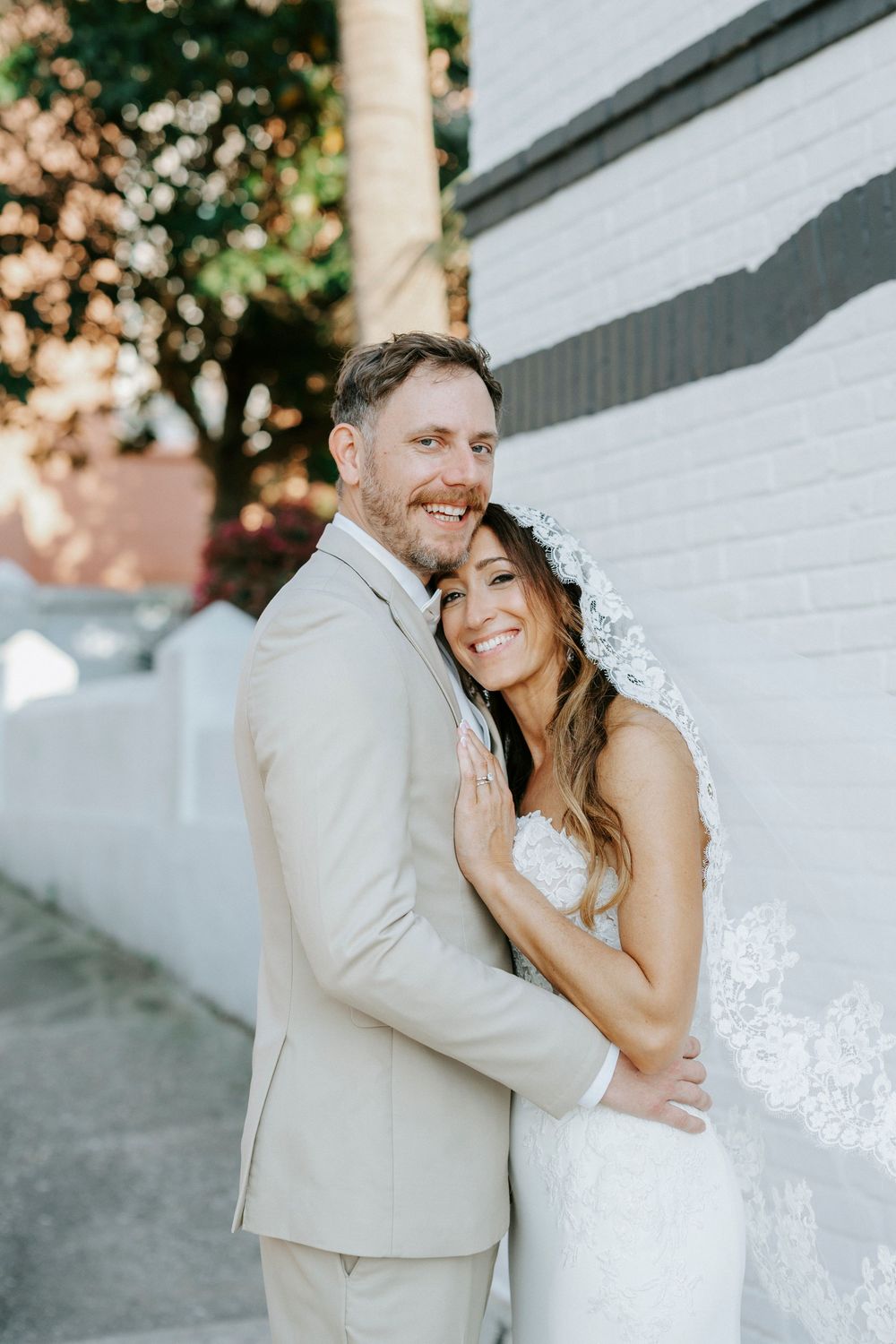 A bride and groom share intimate moments against a white wall in a series of romantic wedding photos.