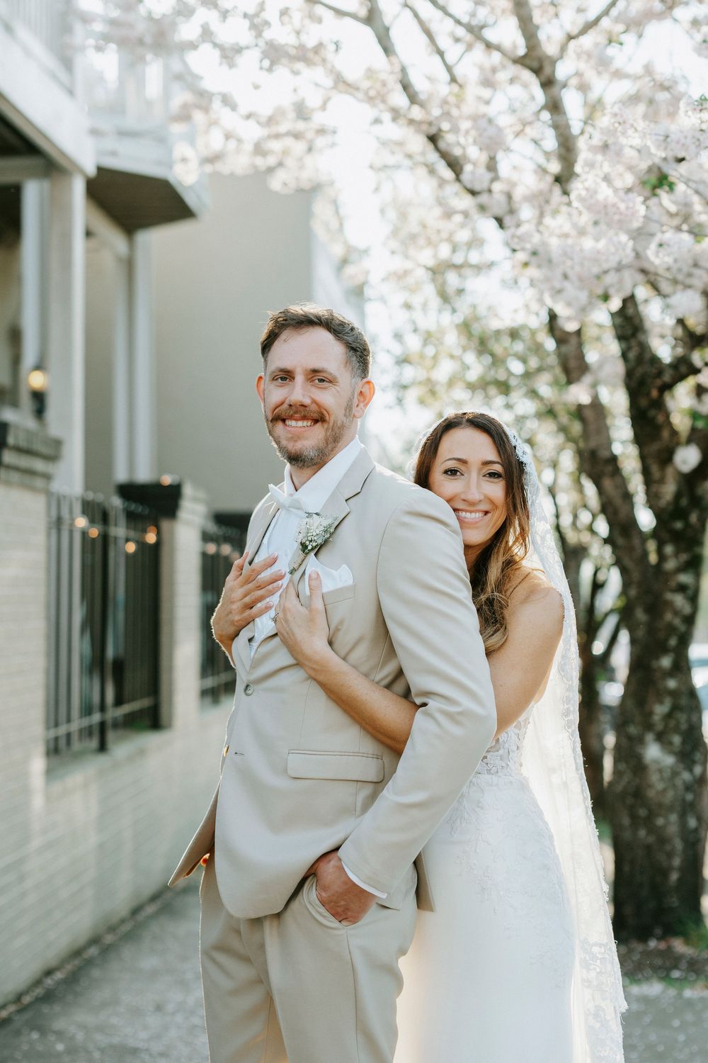 Joyful couple embraces and laughs together under blooming cherry blossom trees on their wedding day.