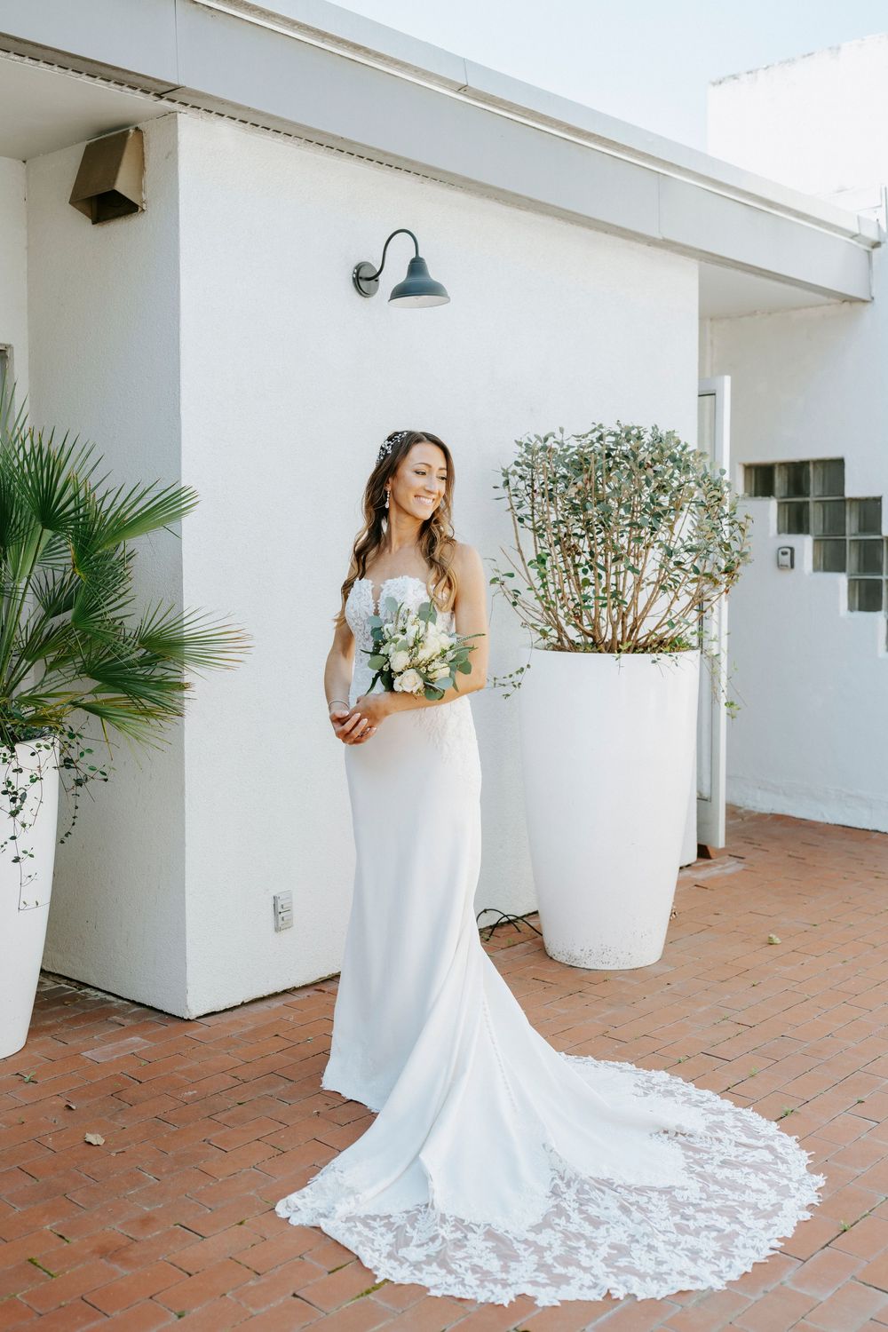 A white wedding dress with lace train flows across terracotta tiles on a Mediterranean-style patio.