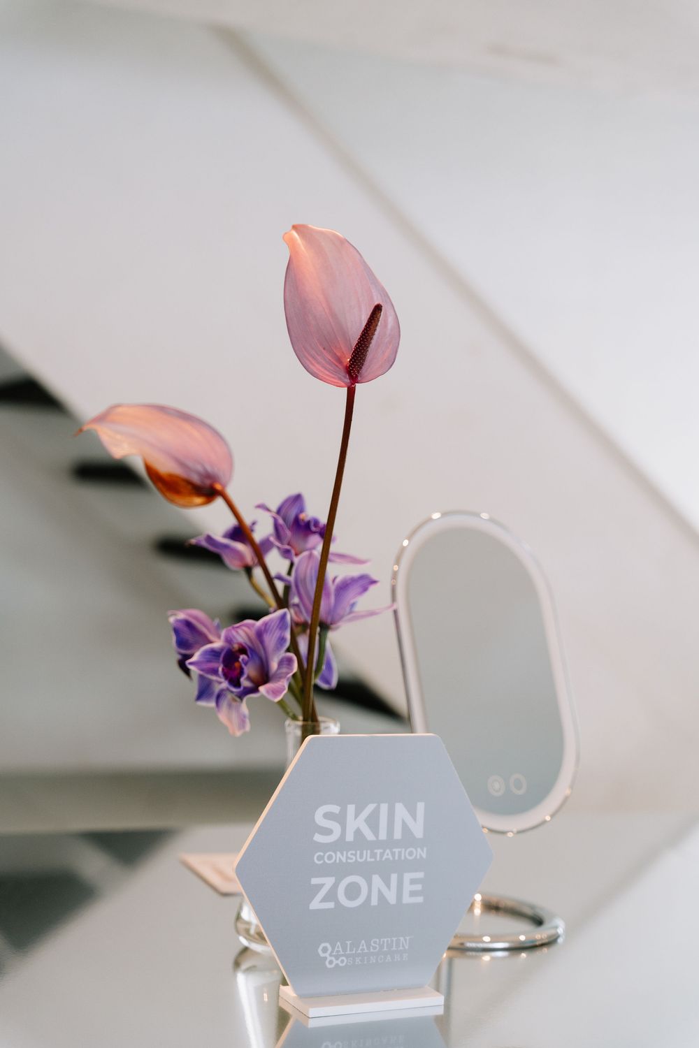 Close-up shot of pink and purple flowers next to a gray sign reading 'SKIN ZONE' in a minimalist setting.