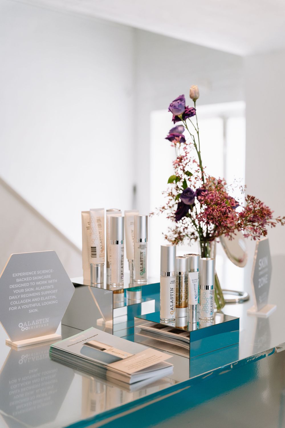 Modern skincare product display with teal accents and delicate floral arrangements in a bright minimalist setting.