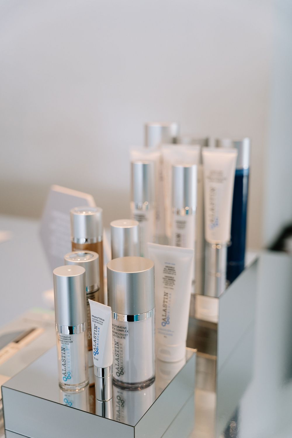 Luxury skincare products arranged in a minimalist display on a reflective surface with white and silver packaging.