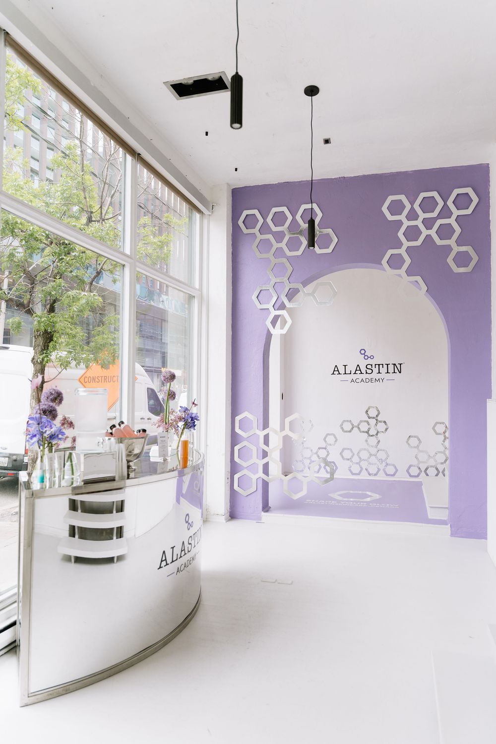 Modern white and purple spa interior with hexagonal wall decor and curved reception desk in minimalist design.