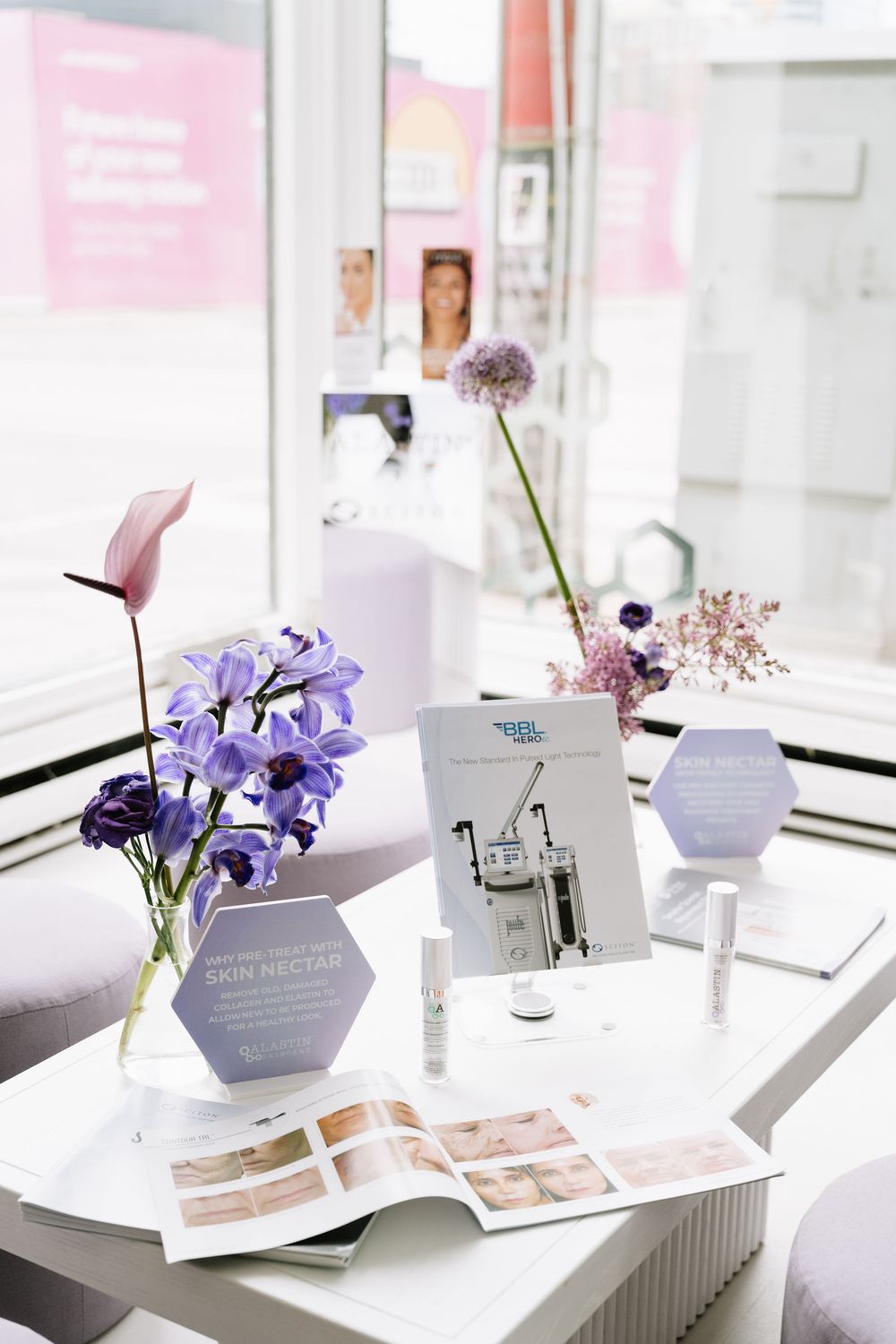 Elegant display of purple flowers and marketing materials on white table with hexagonal branding elements.