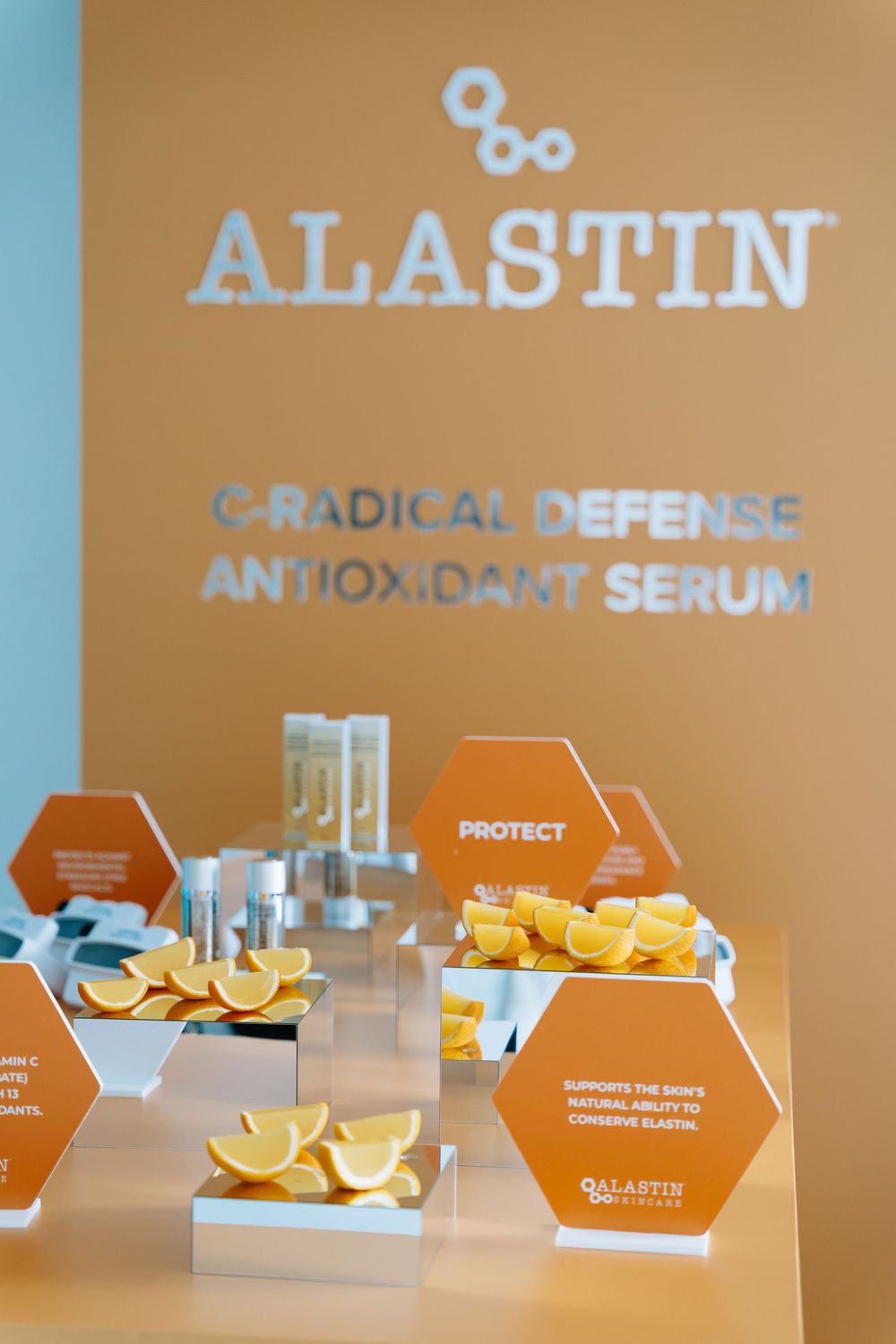 Orange and white product display with Alastin skincare serum packaging and geometric shapes on a clean modern surface.