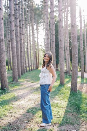 Playful forest photoshoot among tall pine trees wearing denim and casual attire.