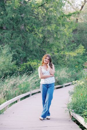 Walking and posing on wooden boardwalk surrounded by lush summer foliage.
