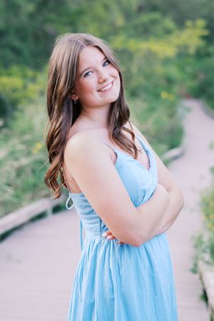Playful poses in light blue sundress on outdoor walking path.