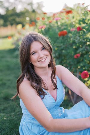 Summer portrait session near blooming red flowers in light blue dress.