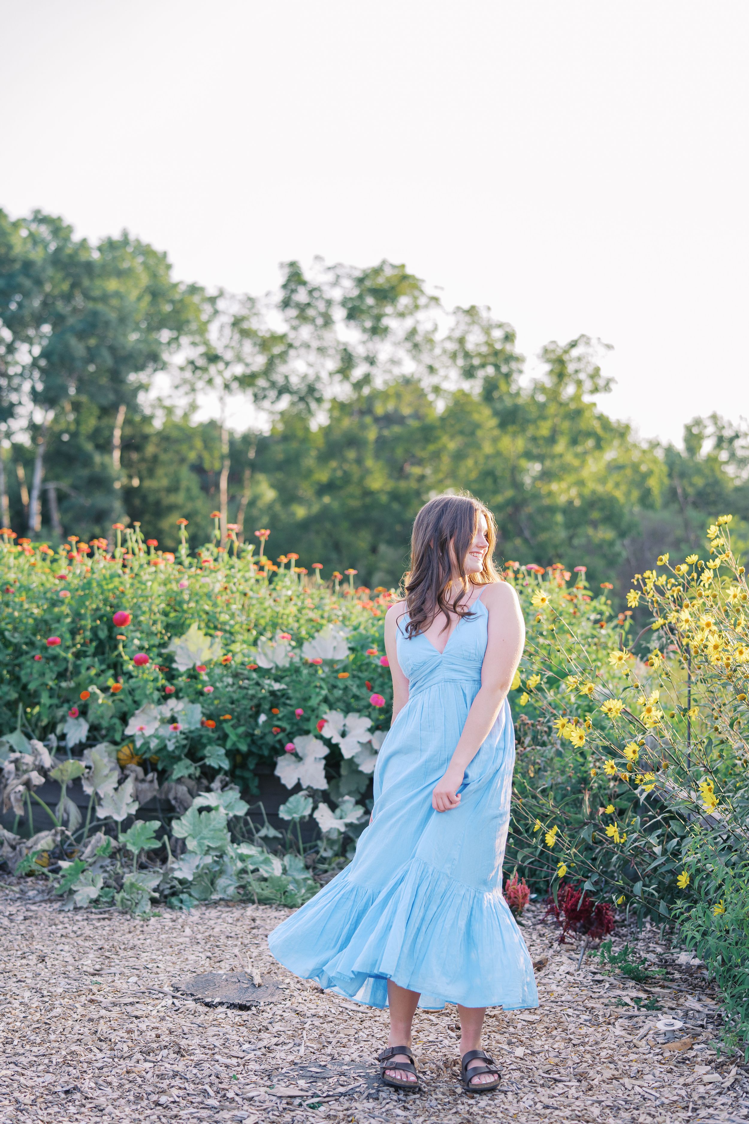 Someone twirling in a light blue dress along a garden path surrounded by colorful flowers.