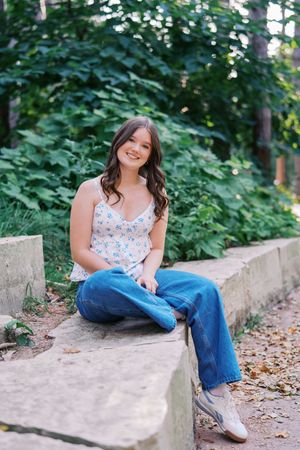 A casual outdoor portrait featuring a floral top and jeans while sitting on concrete steps surrounded by greenery.