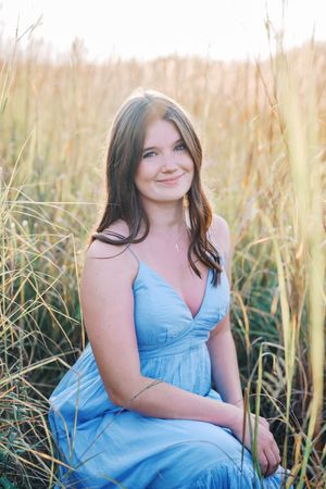Portrait series in a light blue dress against tall golden grass at sunset.