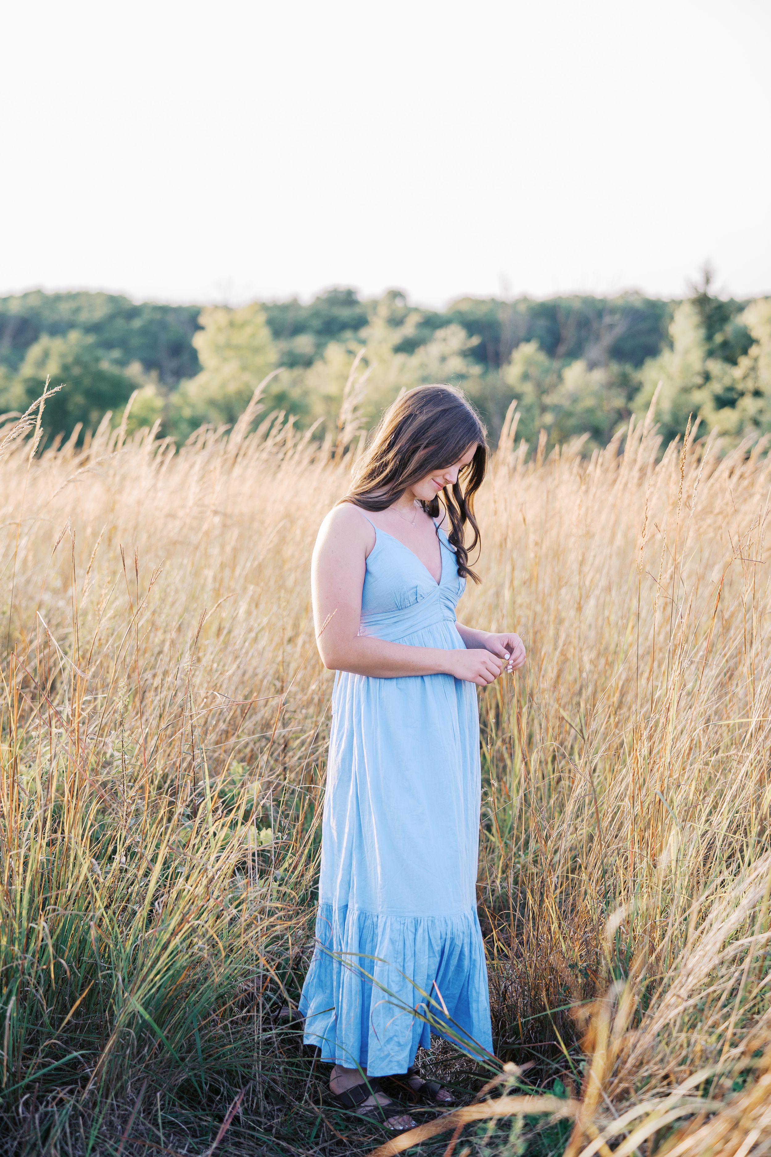 A figure in a flowing blue dress stands among tall golden prairie grass.