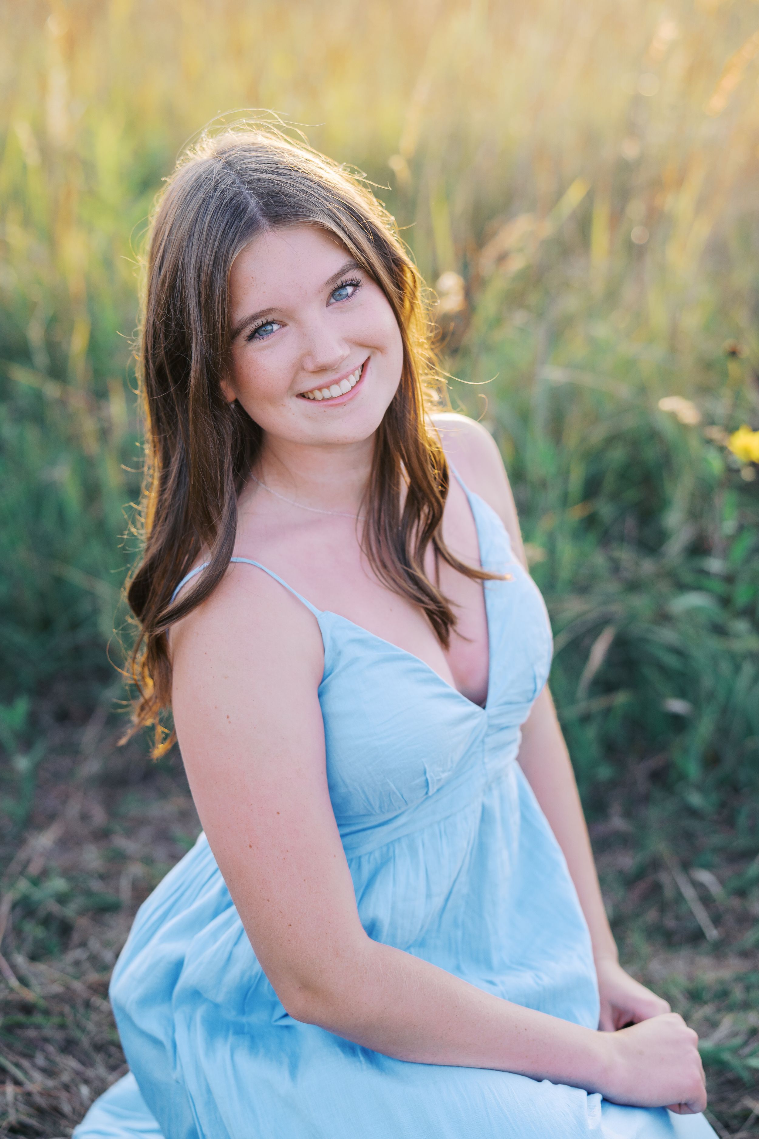 Summer portrait session in a light blue dress surrounded by wild grass and flowers.