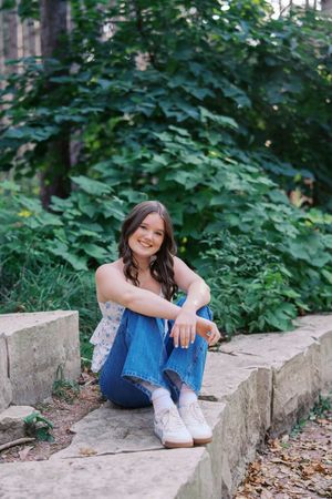 Relaxed outdoor portrait on stone steps with lush green foliage in the background.