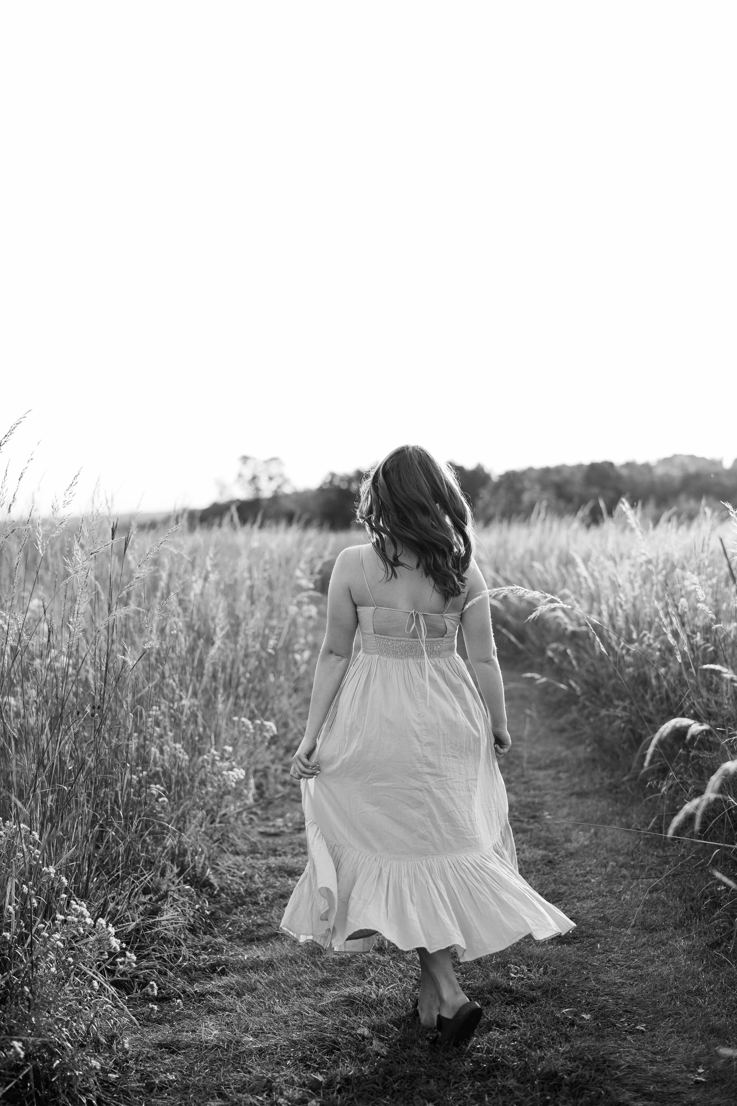 A person in a white dress twirls gracefully through a field at sunset.