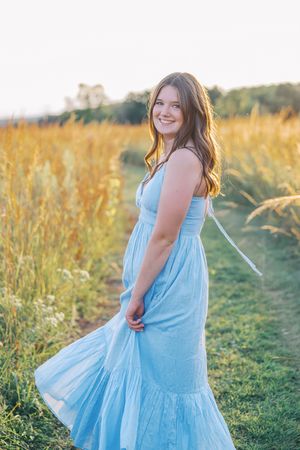 A person wearing a light blue sundress spins joyfully in a sunlit meadow.