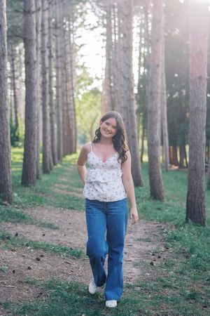 Casual outdoor portrait walking along a tree-lined path wearing a floral top and jeans.