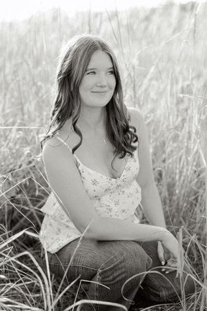 Portrait session in tall grass field wearing white floral top and dark pants.