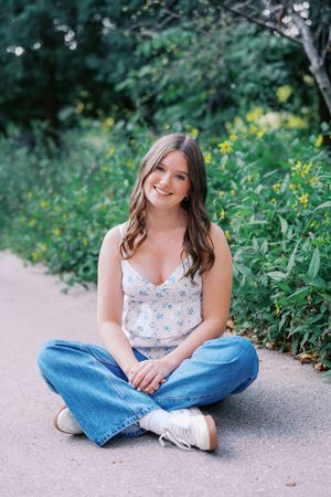 Casual outdoor portraits sitting cross-legged on concrete path surrounded by greenery.