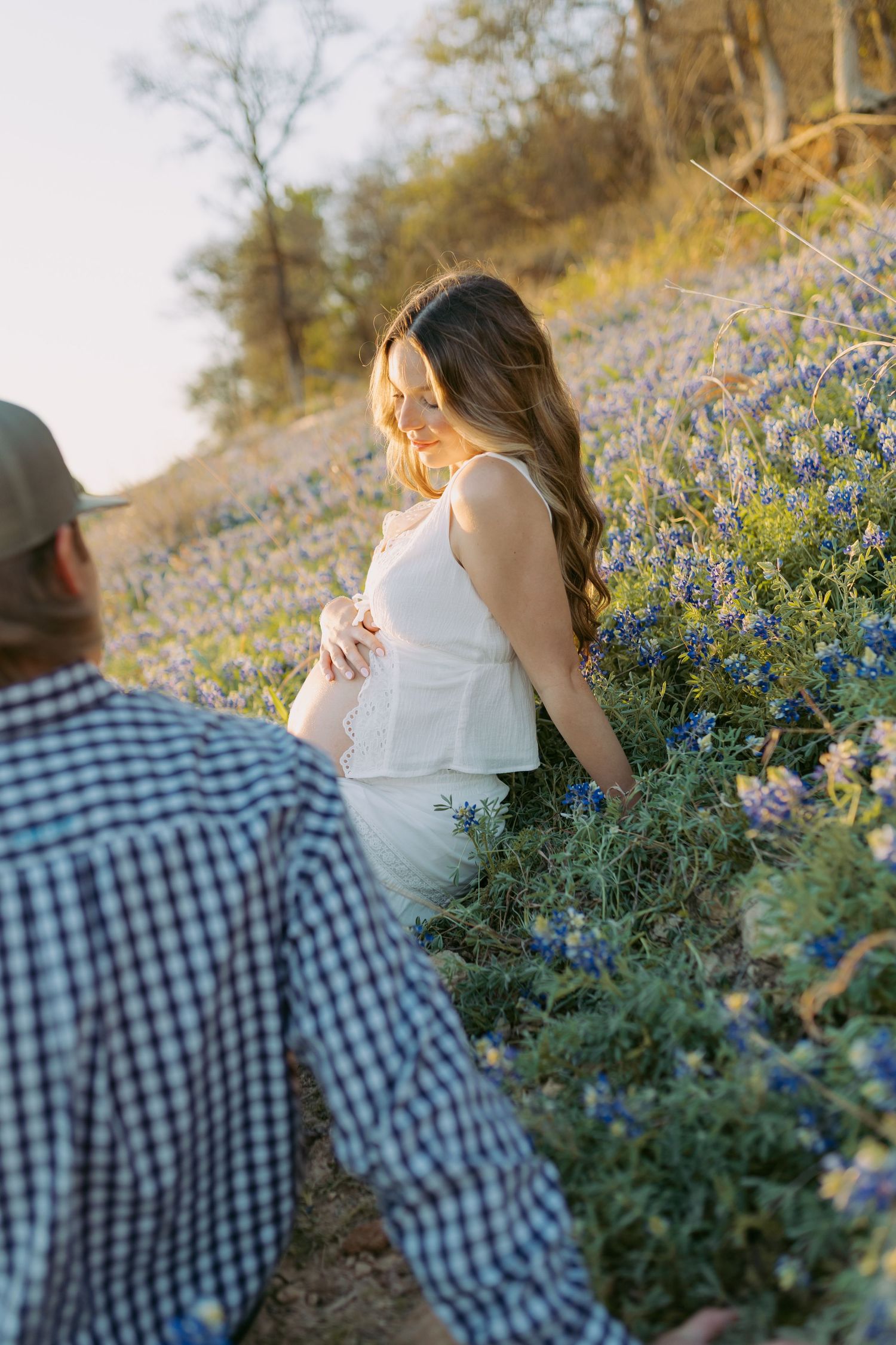 A couple shares a romantic moment among blooming bluebonnets on a hillside during golden hour.