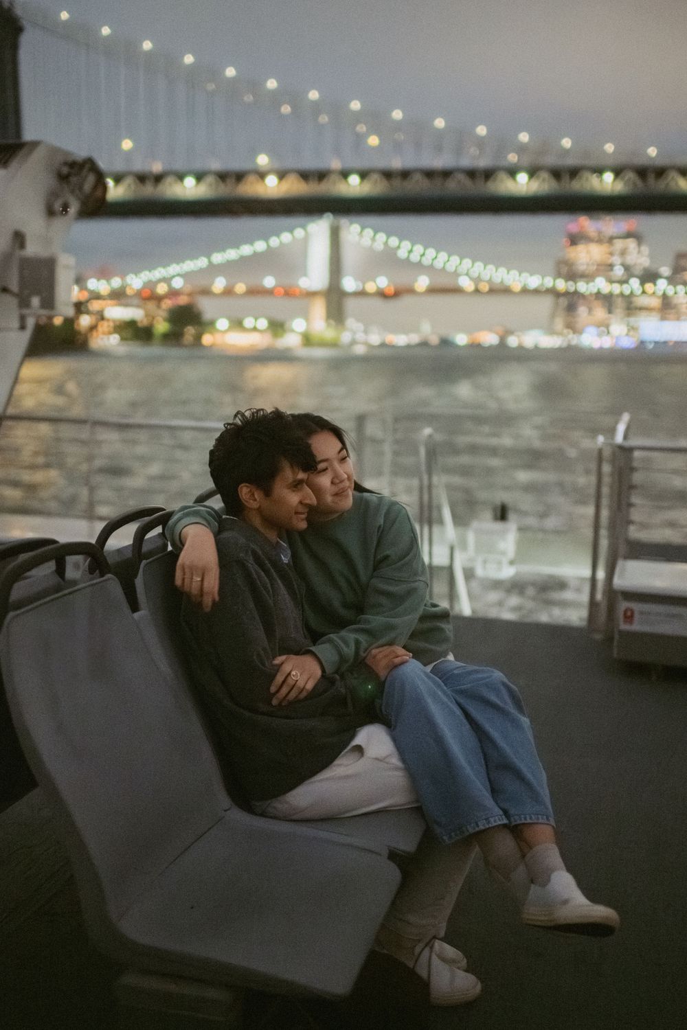A couple rests together on a bench at night with string lights twinkling in the background.
