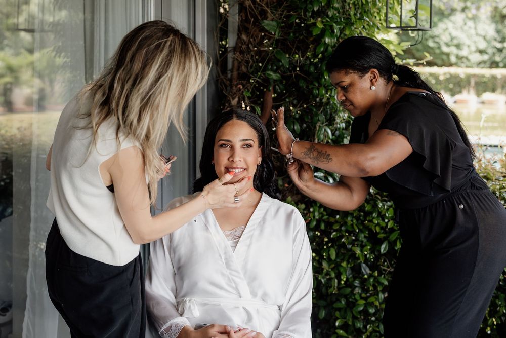 Two stylists work together to prepare a client for a special occasion, styling hair and makeup in an outdoor setting.