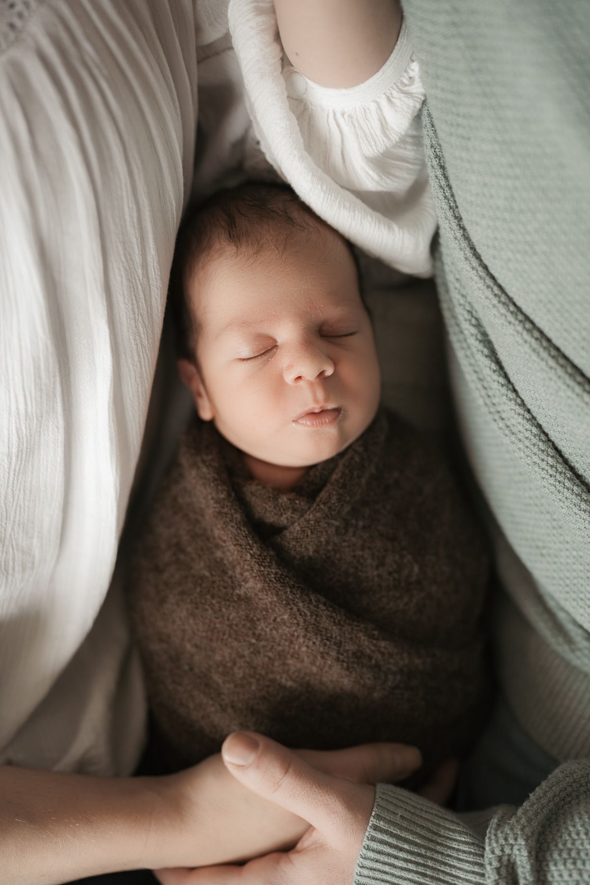 Series of close-up shots showing a sleeping baby wrapped in brown and white blankets.