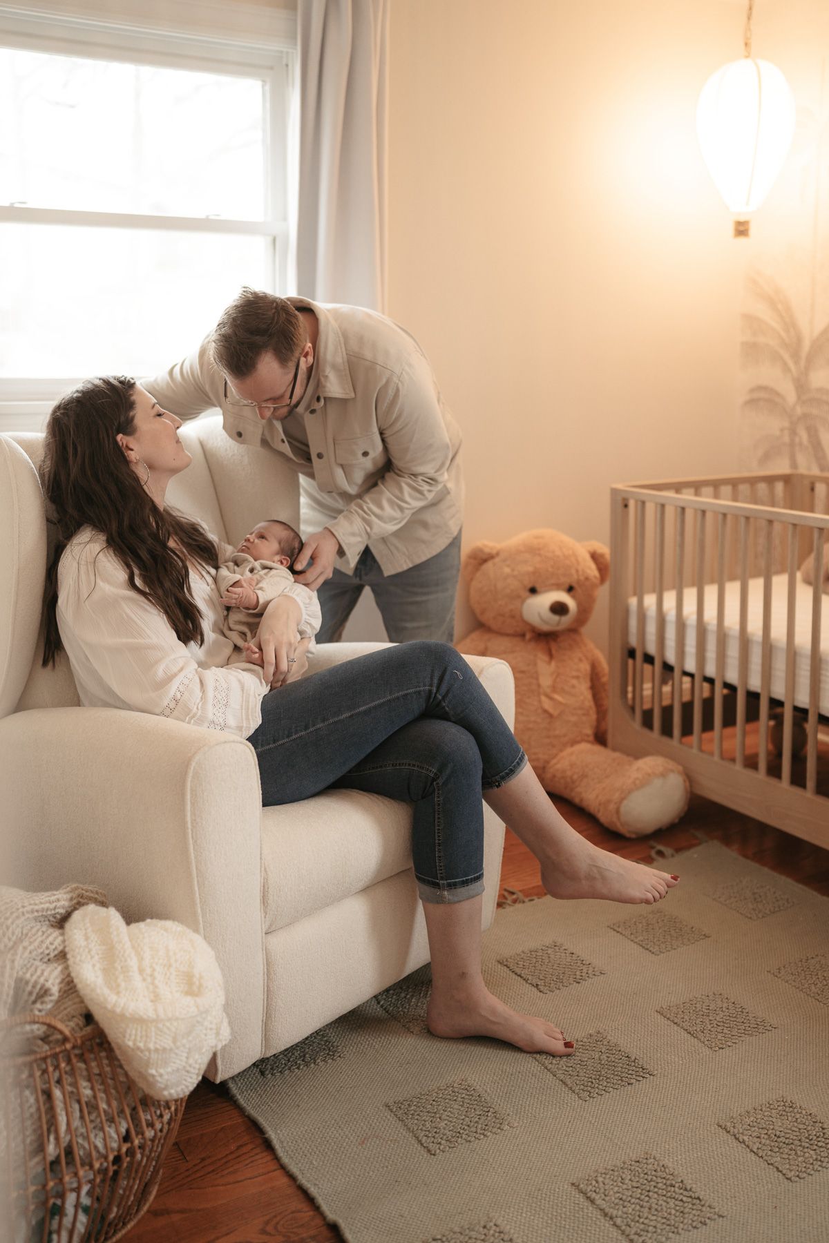 A couple shares intimate moments on a white couch in a nursery with a teddy bear and crib visible in the background.
