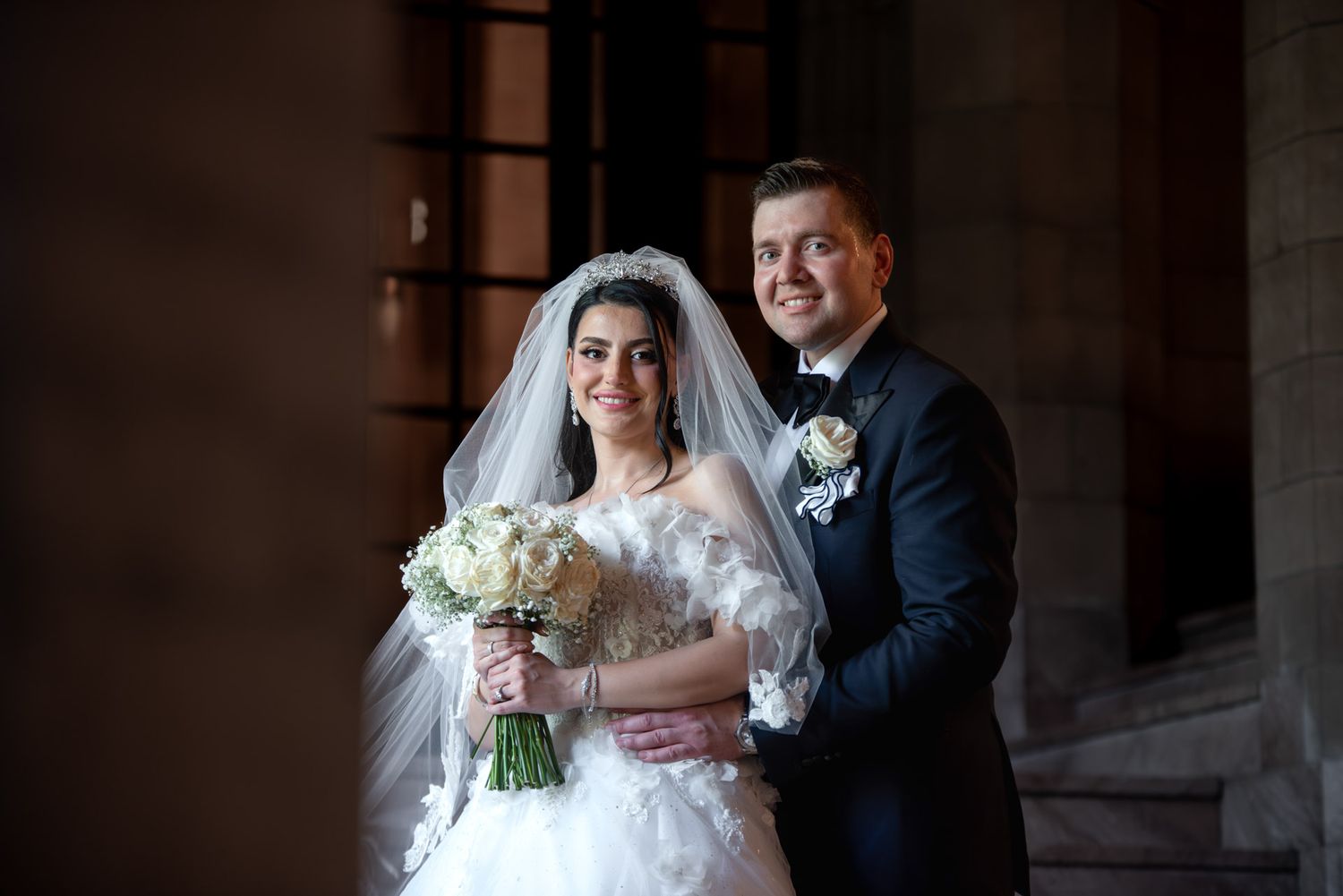 Elegant bride and groom posing together with white bouquet at their wedding ceremony.
