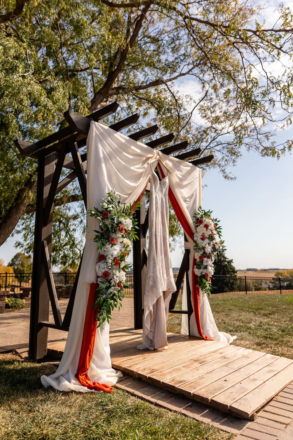 Elegant outdoor wedding arch draped in white fabric and red floral arrangements  at a Venue on the Ridge in Elkhorn, NE