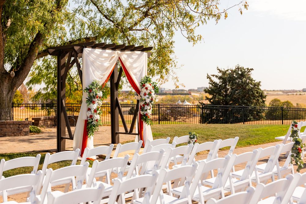 Outdoor wedding ceremony setup with white chairs & a wooden arch decorated with floral arrangements at a Venue on the Ridge in Elkhorn, NE