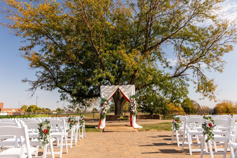 Outdoor wedding ceremony setup with white chairs, floral arch, and large tree backdrop on a sunny day  at a Venue on the Ridge in Elkhorn