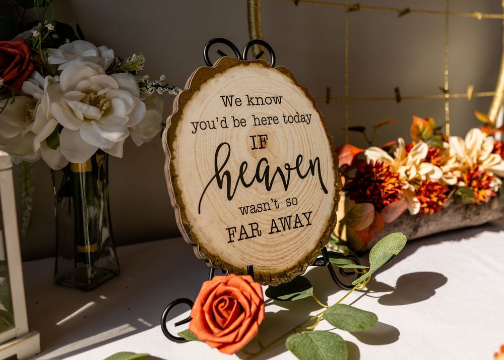 Rustic wood slice sign reading 'We know you'd be here today if heaven wasn't so far away' with floral decor.