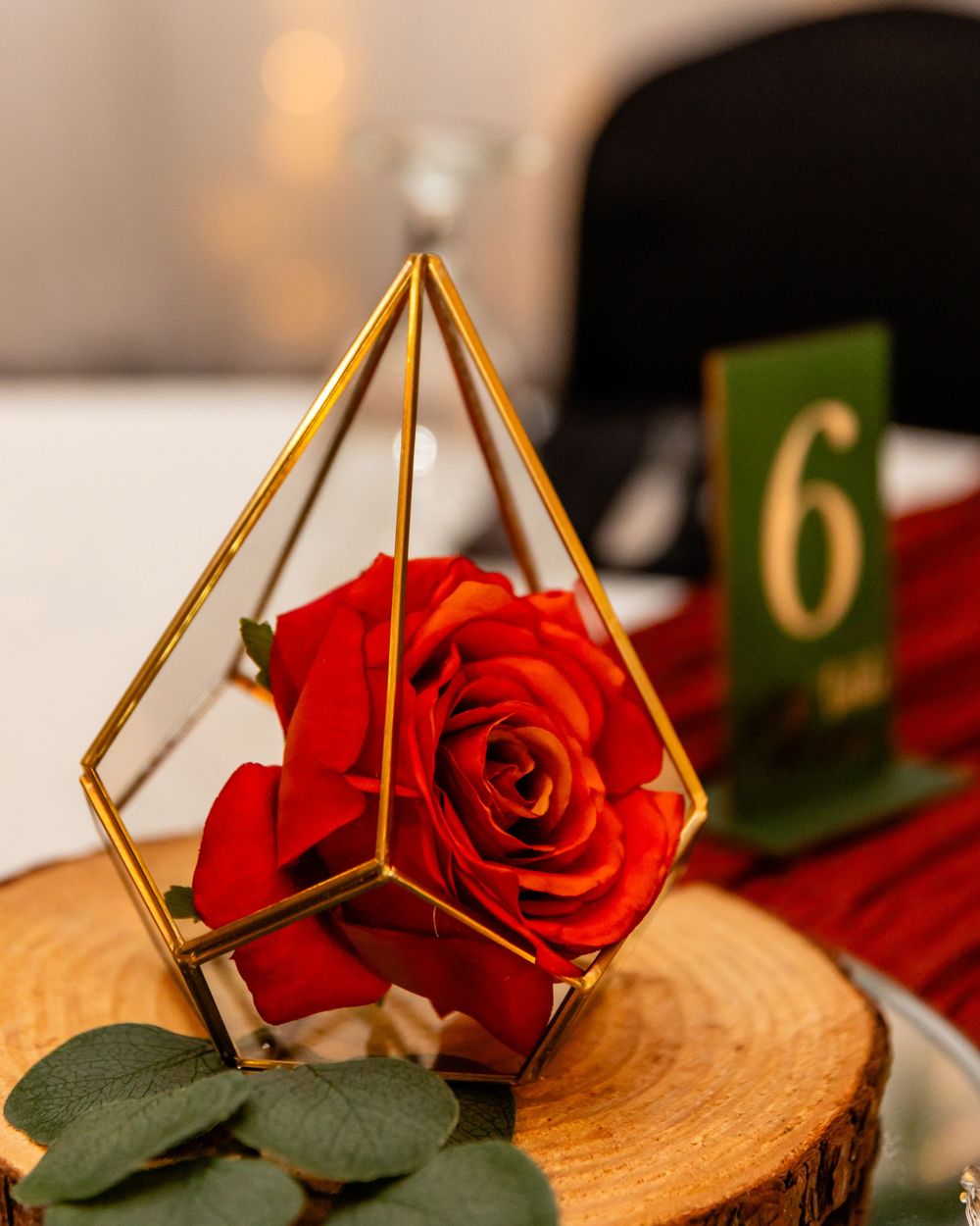 Red rose in a gold geometric terrarium centerpiece on a wood slice with a table number six sign.