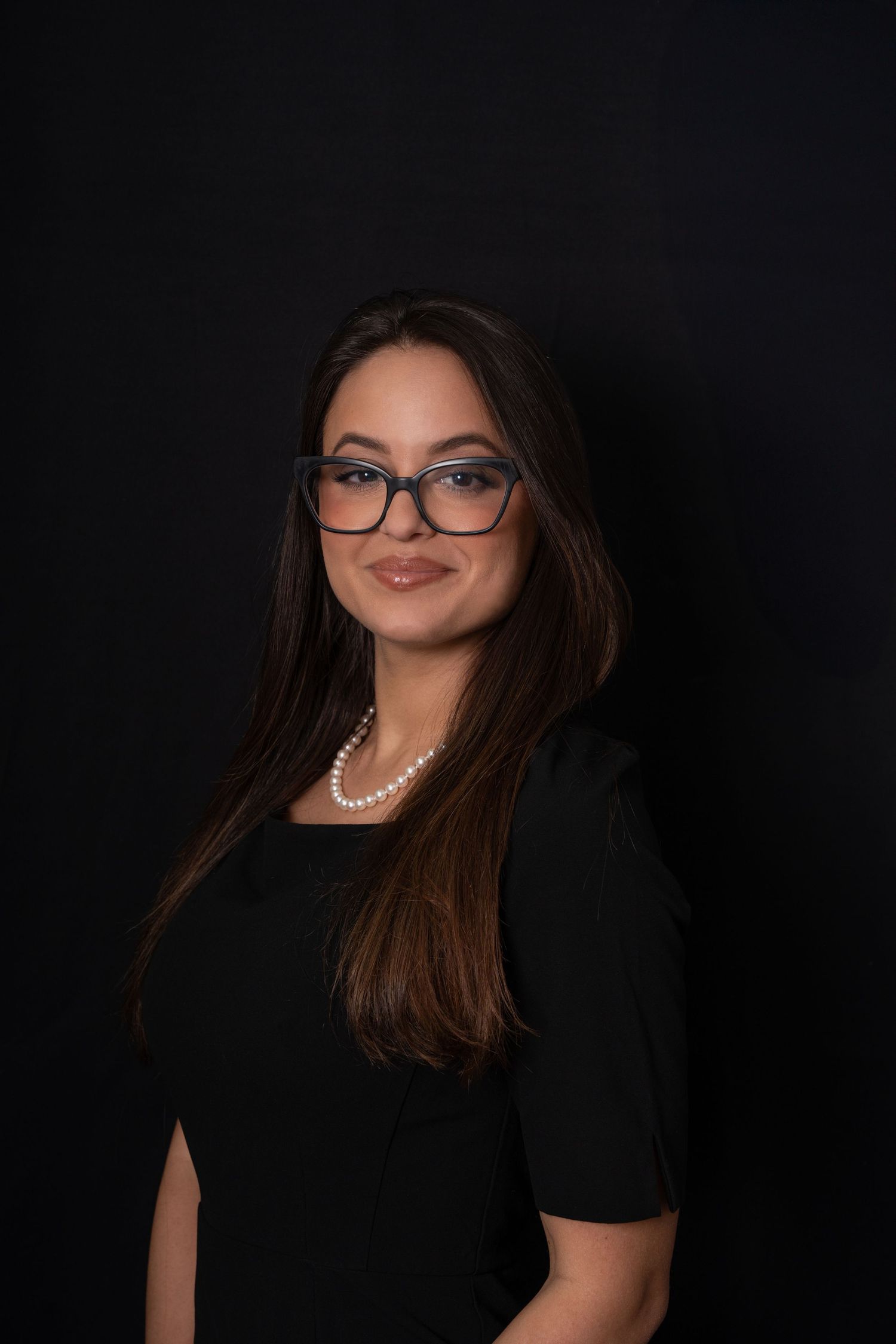 A women with glasses poses for a headshot on a black background.