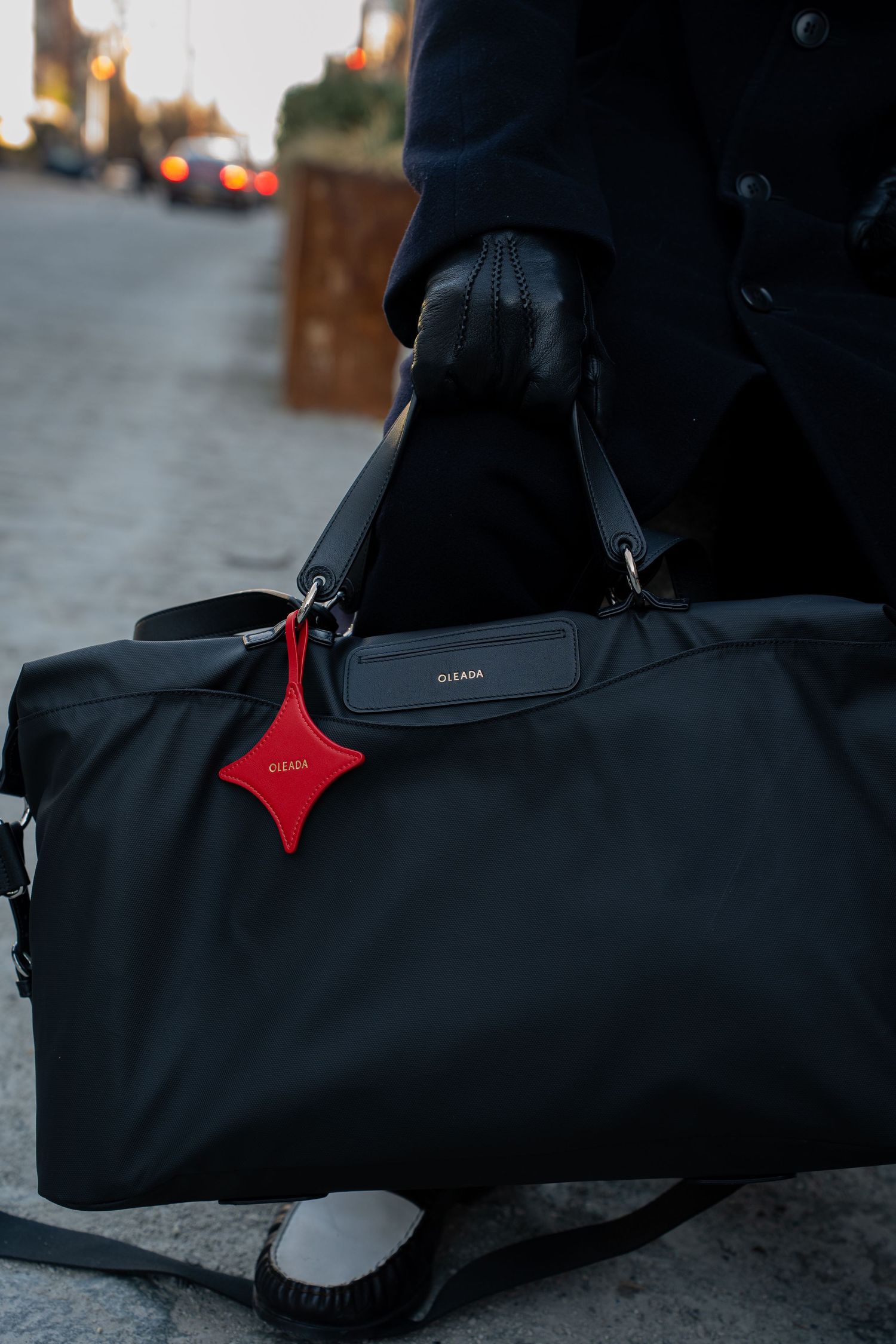 Close-up of black nylon duffle bag with red star charm tag held by gloved hands outdoors.