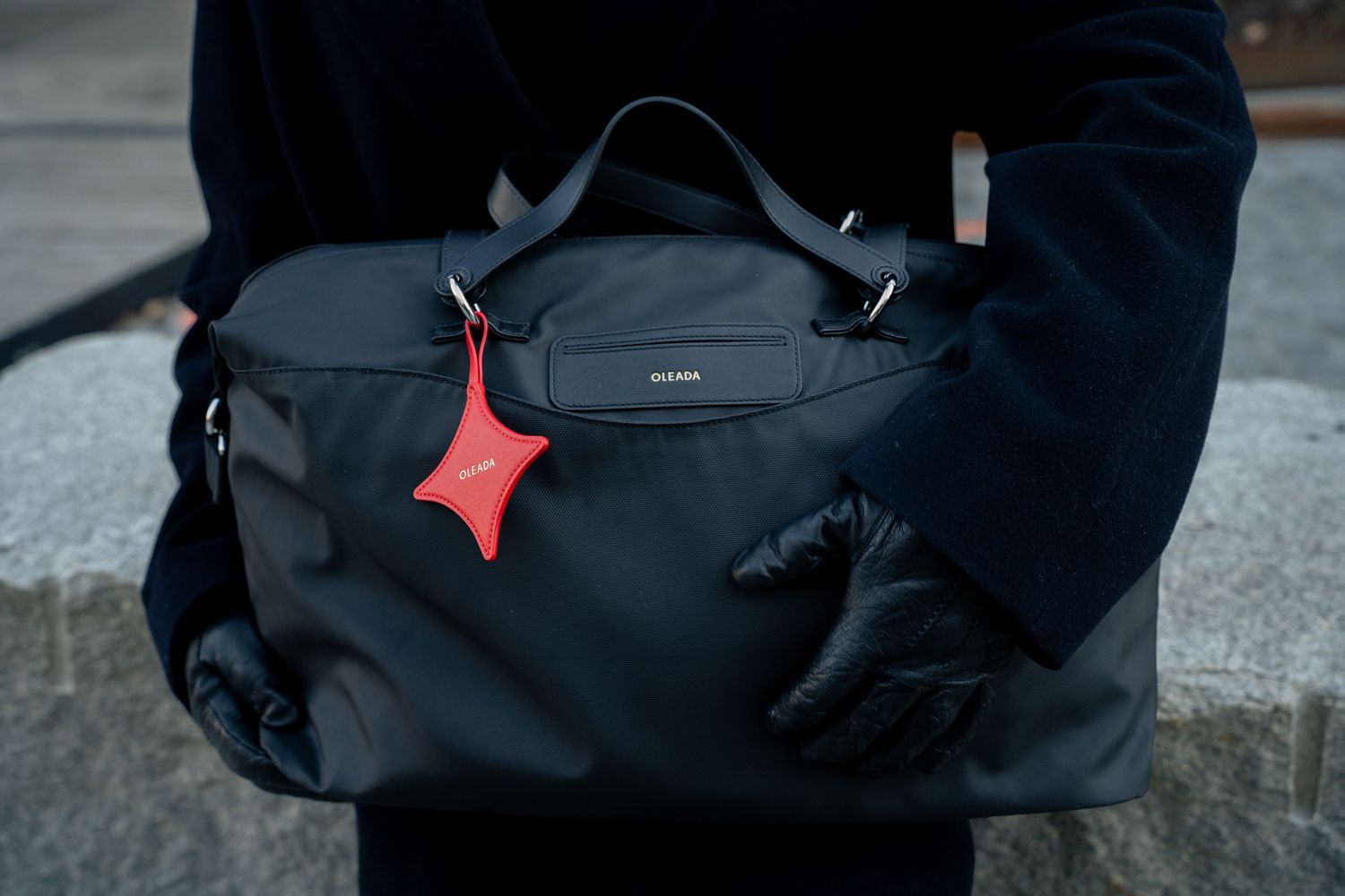 Person in navy coat holding black nylon duffle bag with distinctive red star charm keychain.