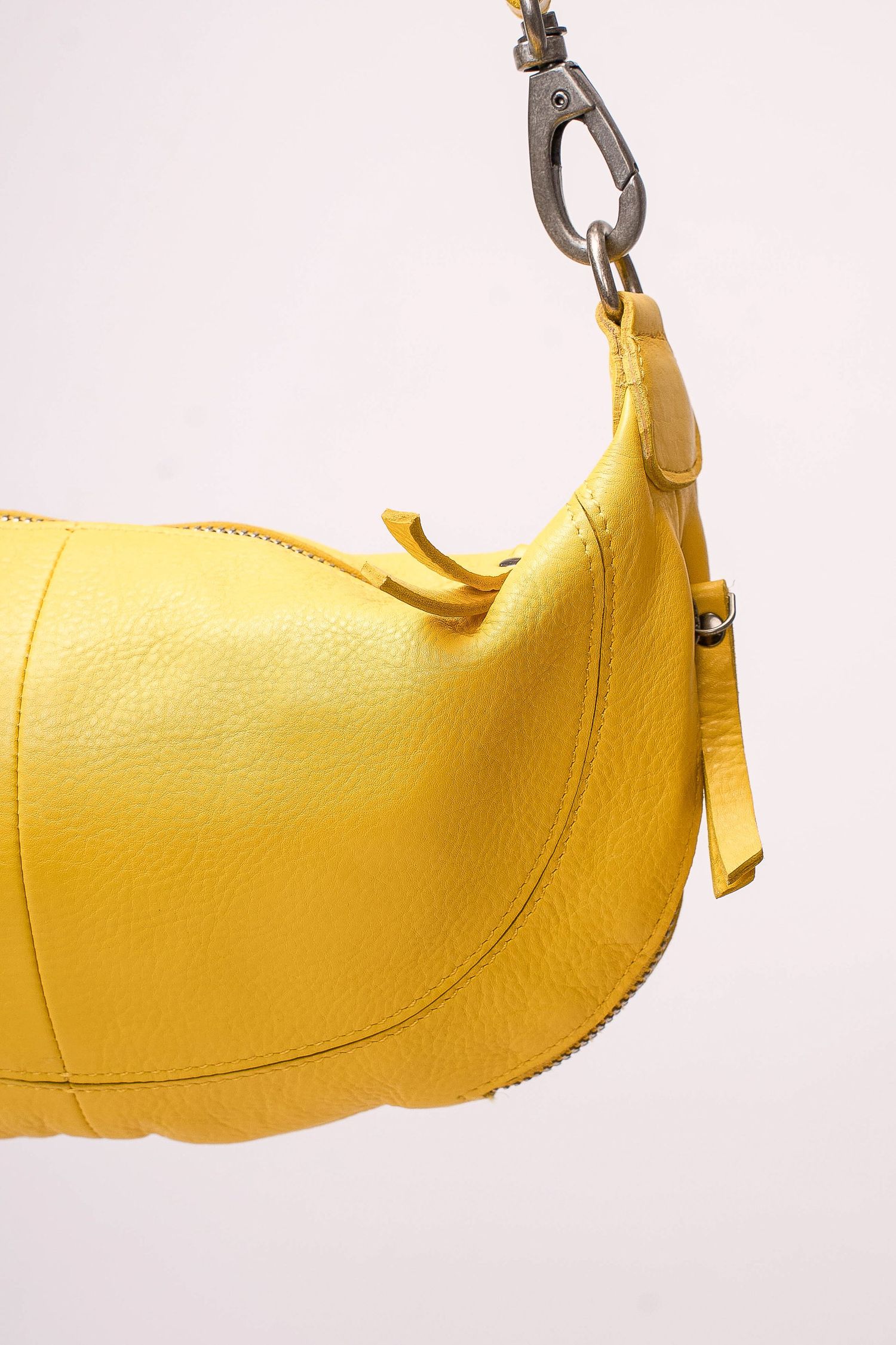 Close-up of yellow leather hobo bag with silver carabiner clasp hardware on white background.