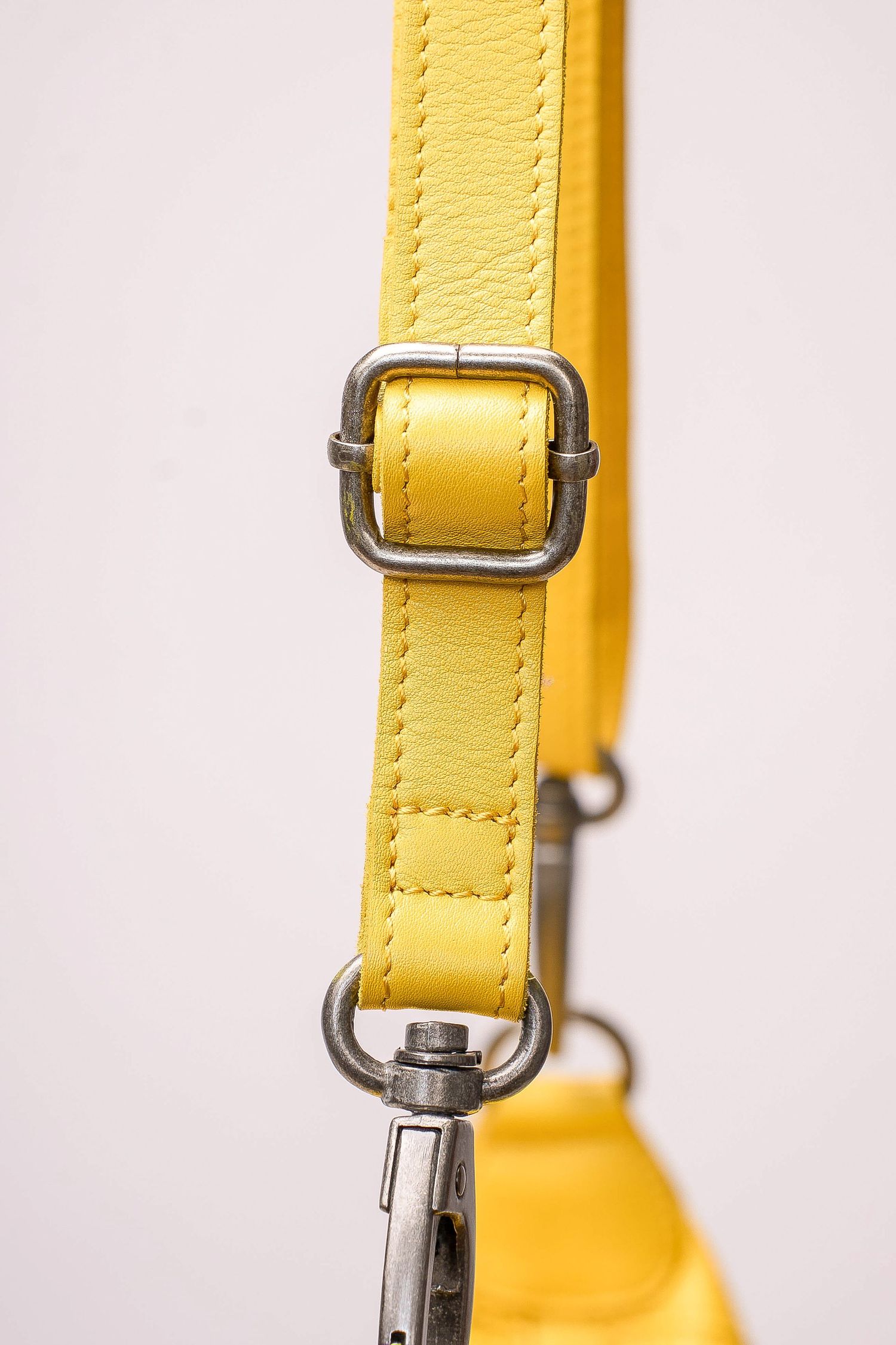 Detailed view of yellow leather bag strap with silver buckle and adjustable hardware on white background.