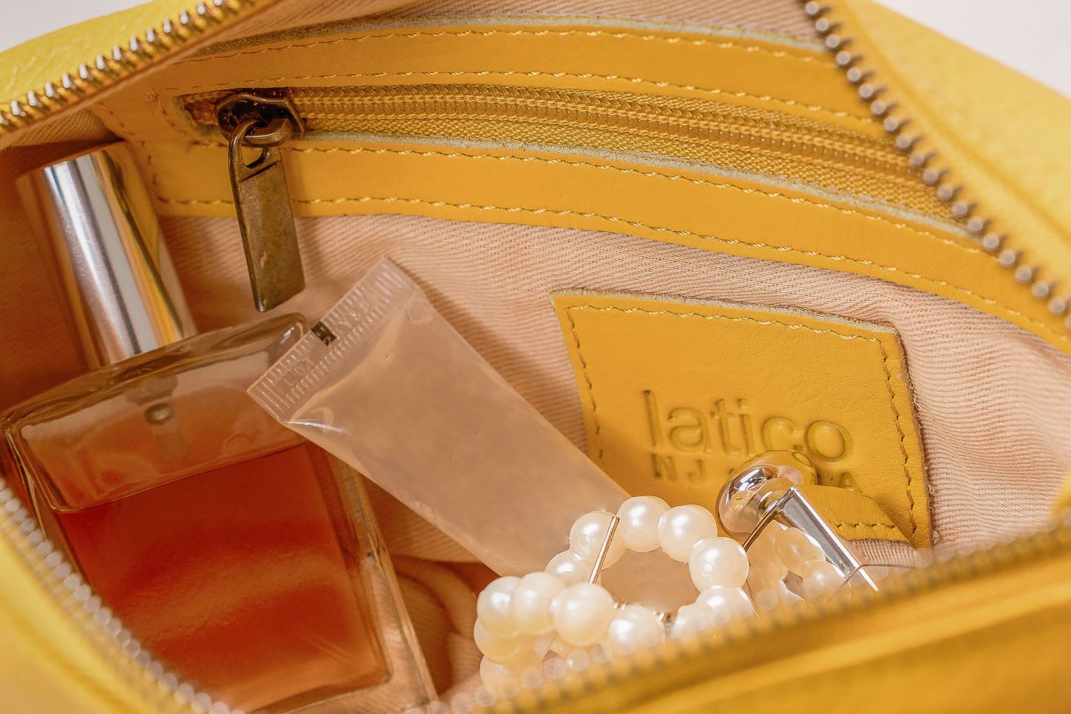 Open yellow leather bag interior showing perfume, pearls, and latico brand label.