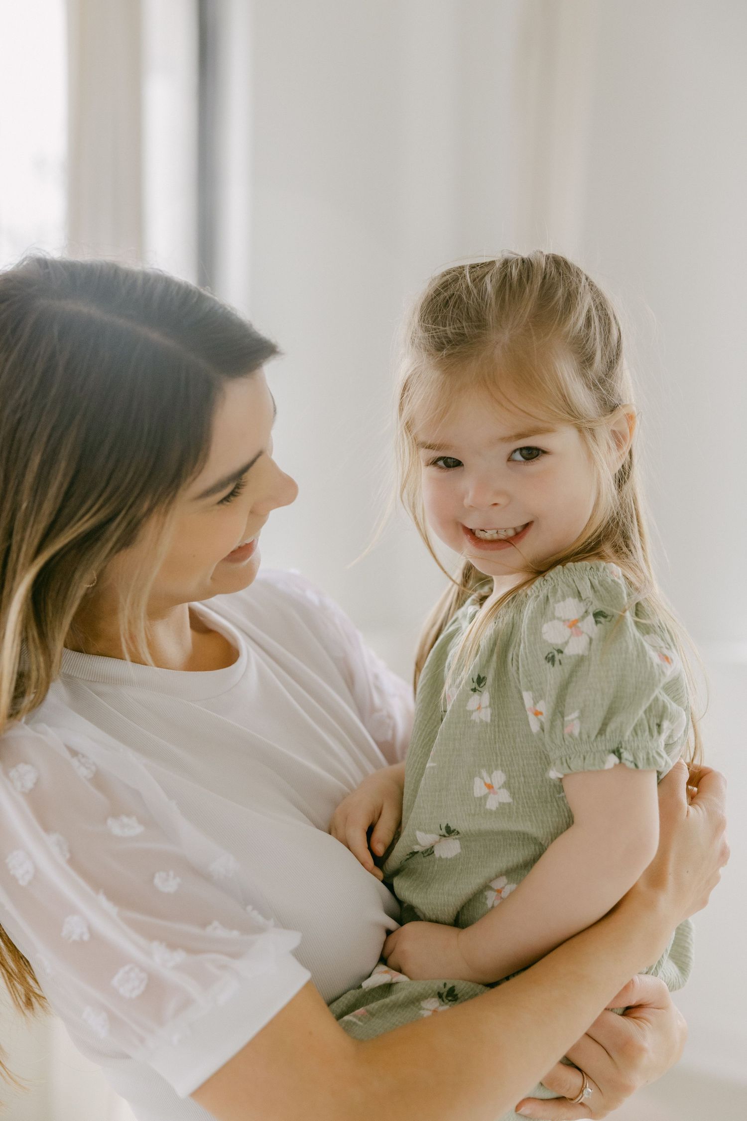 A tender moment between parent and child sharing laughter and cuddles in a bright, airy room.